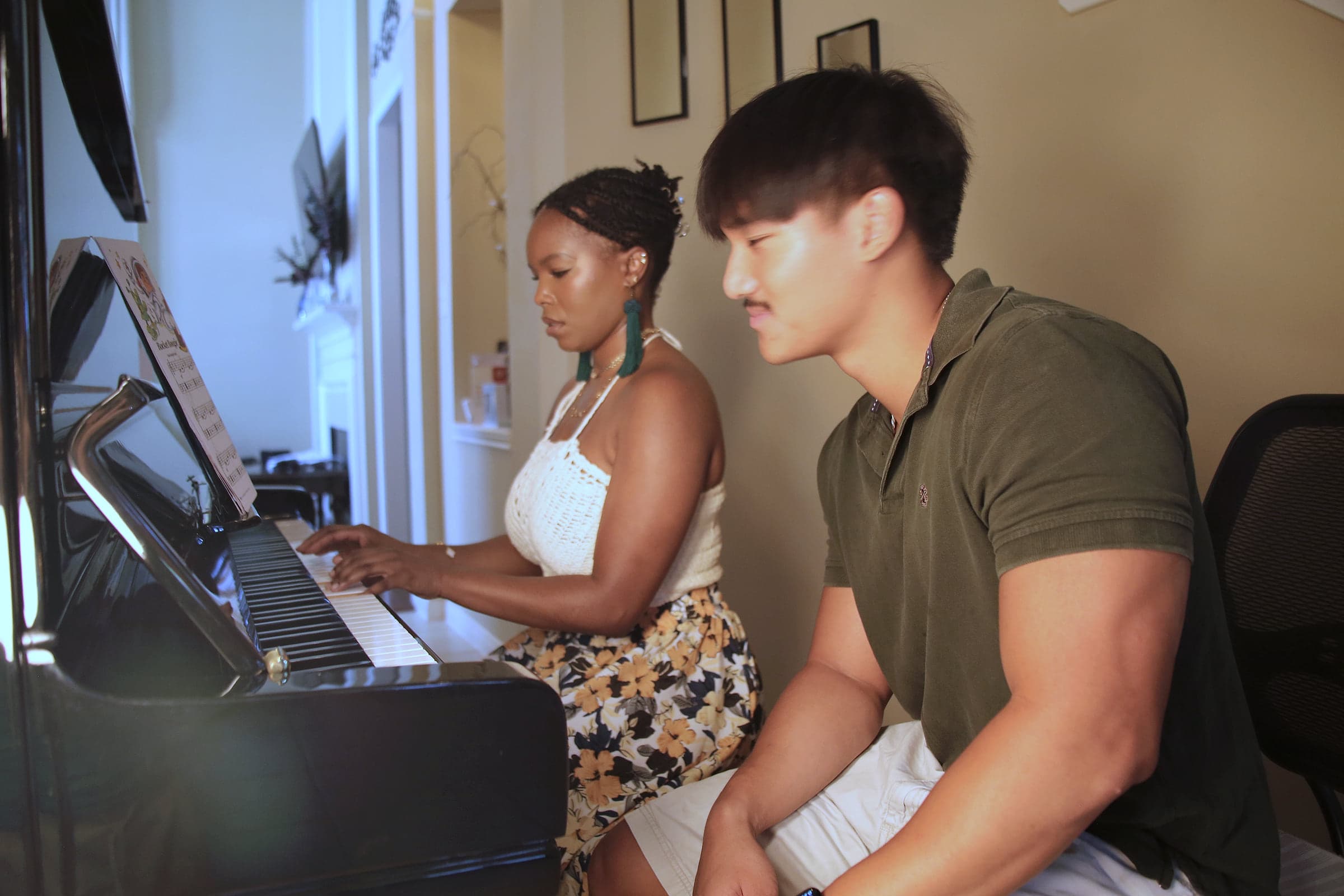 An adult student playing the piano while Preston listens beside her