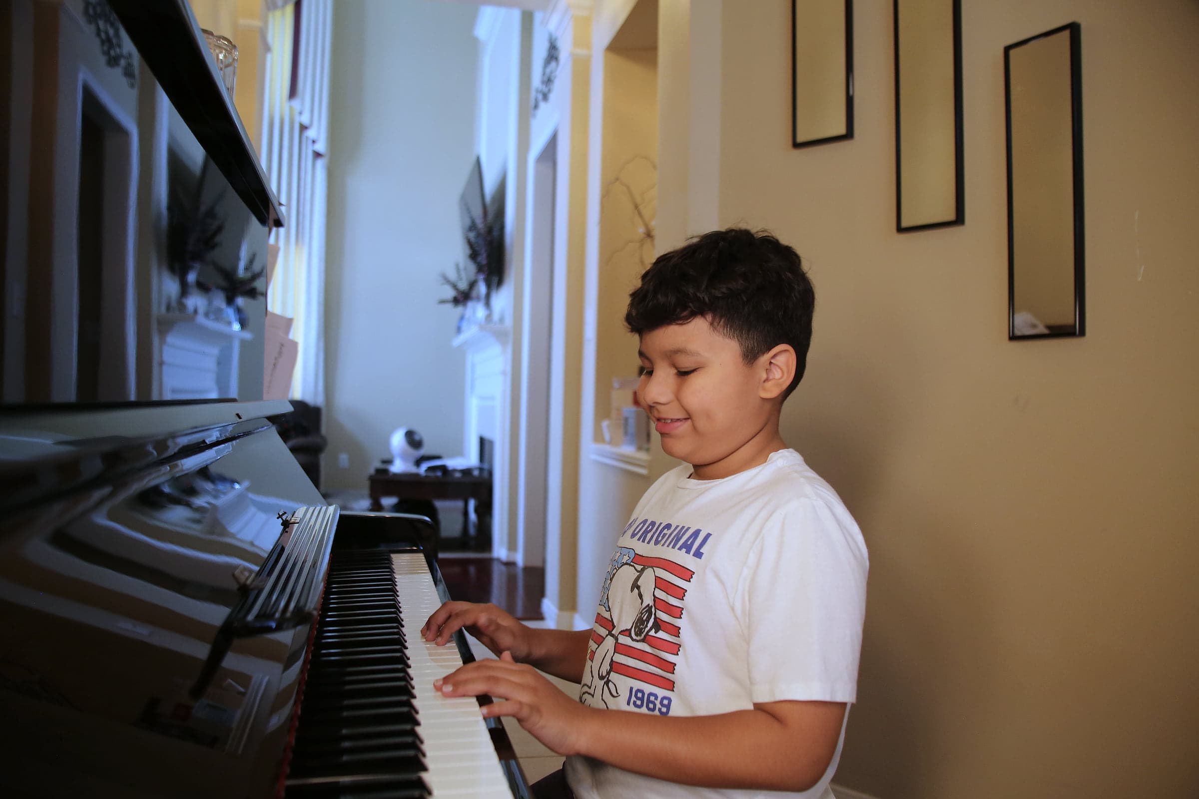 A young boy playing an upright piano and smiling
